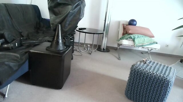 Latex masked person enjoys sitting on giant sextoy plug