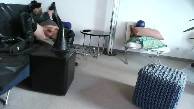 Latex masked person enjoys sitting on giant sextoy plug