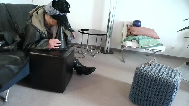 Latex masked person enjoys sitting on giant sextoy plug