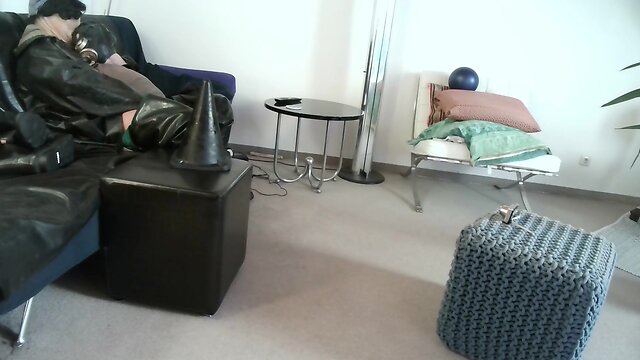 Latex masked person enjoys sitting on giant sextoy plug