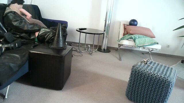 Latex masked person enjoys sitting on giant sextoy plug