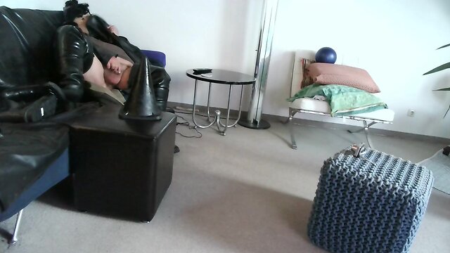 Latex masked person enjoys sitting on giant sextoy plug