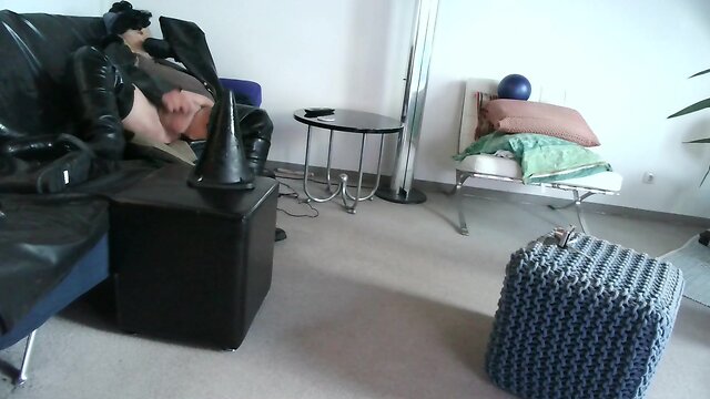 Latex masked person enjoys sitting on giant sextoy plug